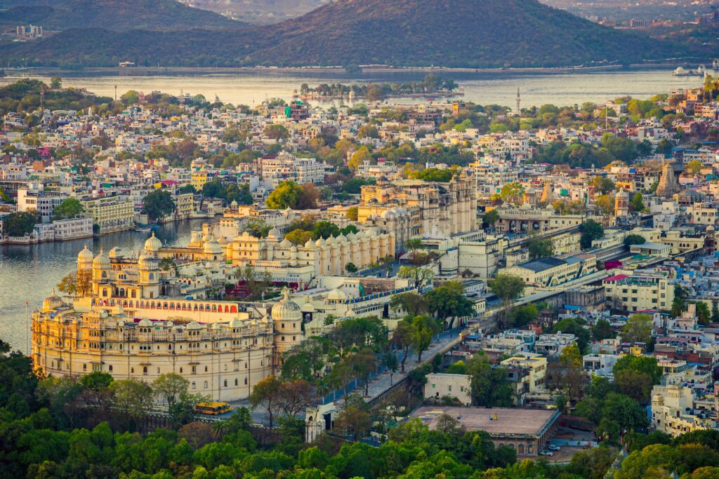 Aerial view of the historic Udaipur City Palace and surrounding cityscape against a tranquil lake backdrop. (Luxury Travel in Rajasthan)