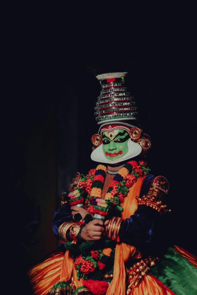 Vibrant portrait of a Kathakali performer in traditional attire showcasing intricate makeup and costume against a dark background.