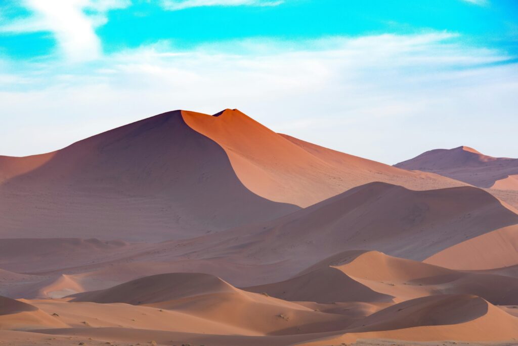 Capture the serene beauty of Namibian sand dunes under a vibrant sky. Perfect for desert-themed designs.