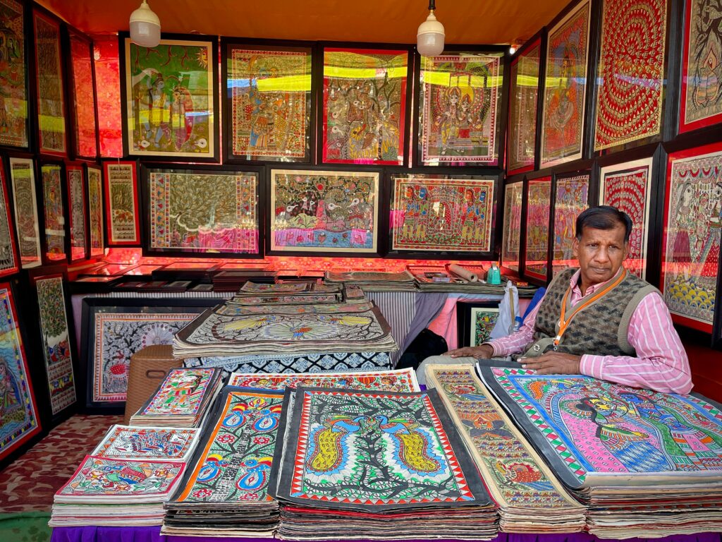 Artisan selling vibrant traditional paintings at a market stall.