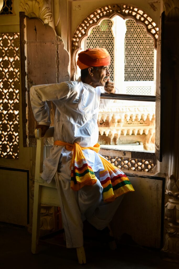 A Rajasthani man in traditional attire gazing out of an ornate window in Jodhpur, India.