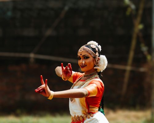 Portrait of a traditional Indian woman performing a cultural dance in vibrant attire outdoors.