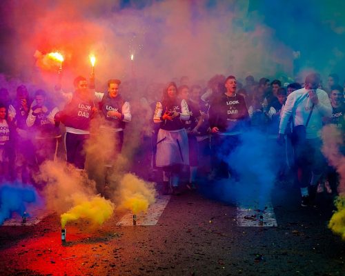 A lively group celebrating at night with color smoke bombs in a street festival.